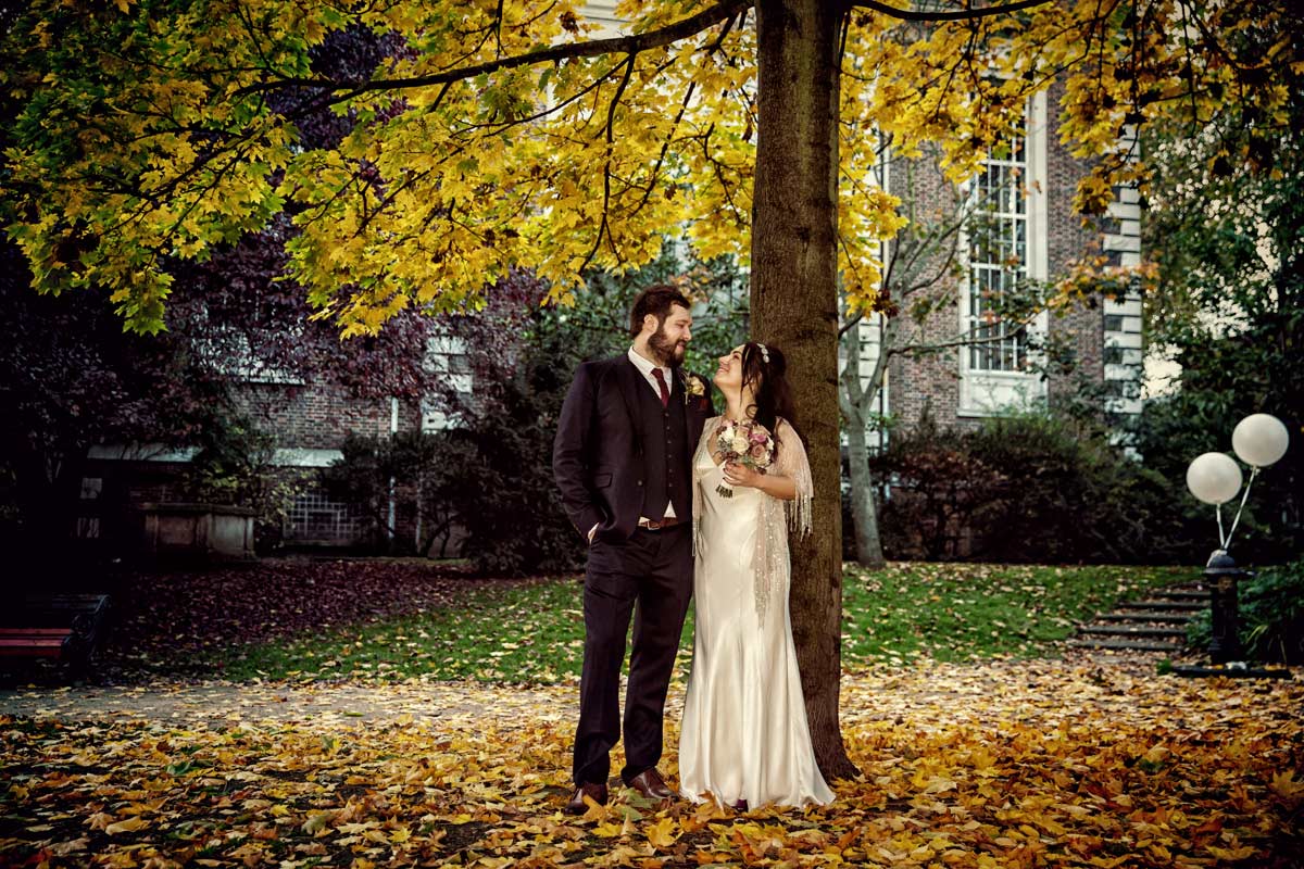 couple chat by tree and autumn leaves after their Islington wedding