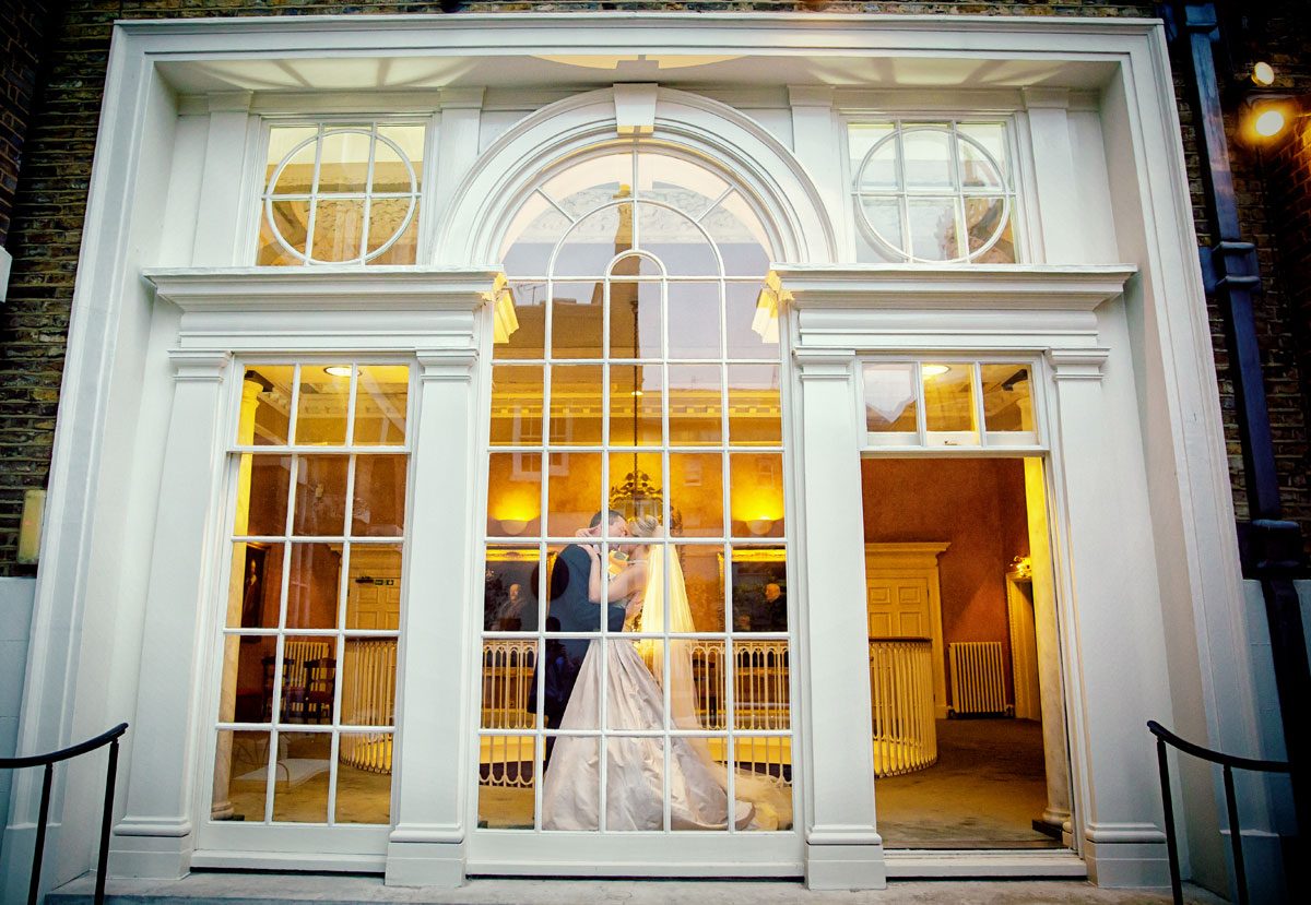 Couple kiss in front of window at Skinners Hall wedding reception