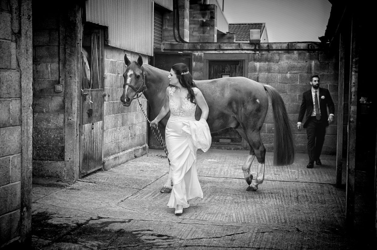 Chelsea-bride-leads-horse-in-stables-on-wedding-day-image