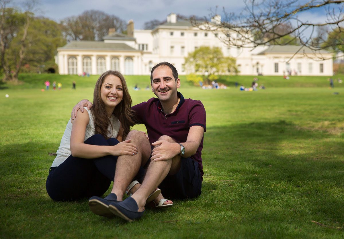 Engagement couple sit on grass at Kenwood House photo shoot