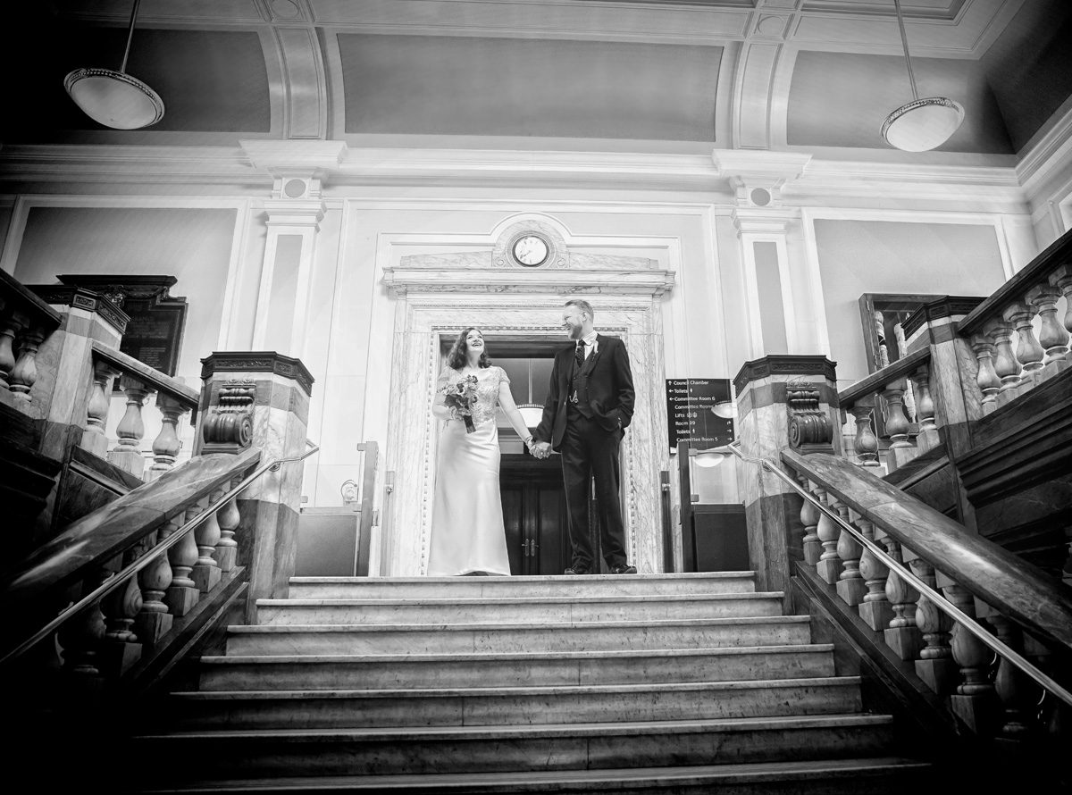 Bride and groom laugh at the top of Islington Town Hall stairs