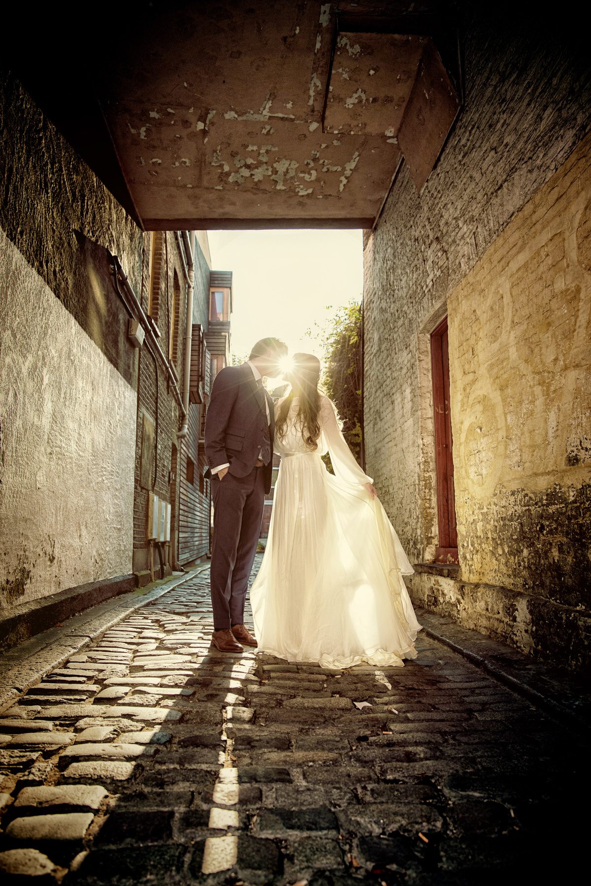 London wedding couple kiss in cobbled alley with sun flare
