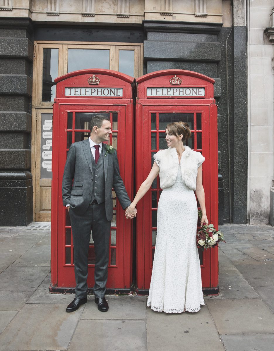 Bride and groom hold hands by red London phone boxes