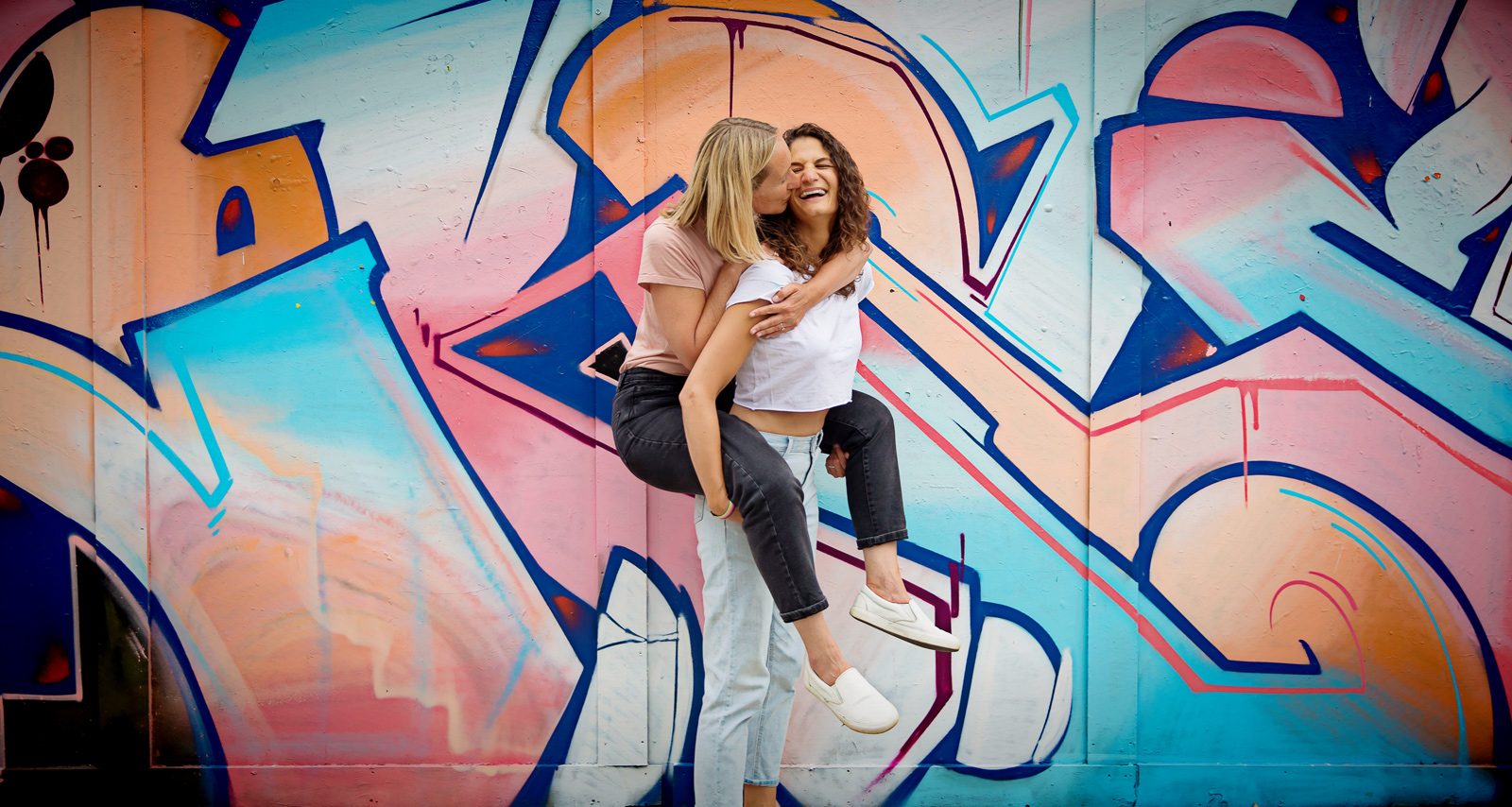 Shoreditch engagement shoot couple piggyback and laugh by graffiti