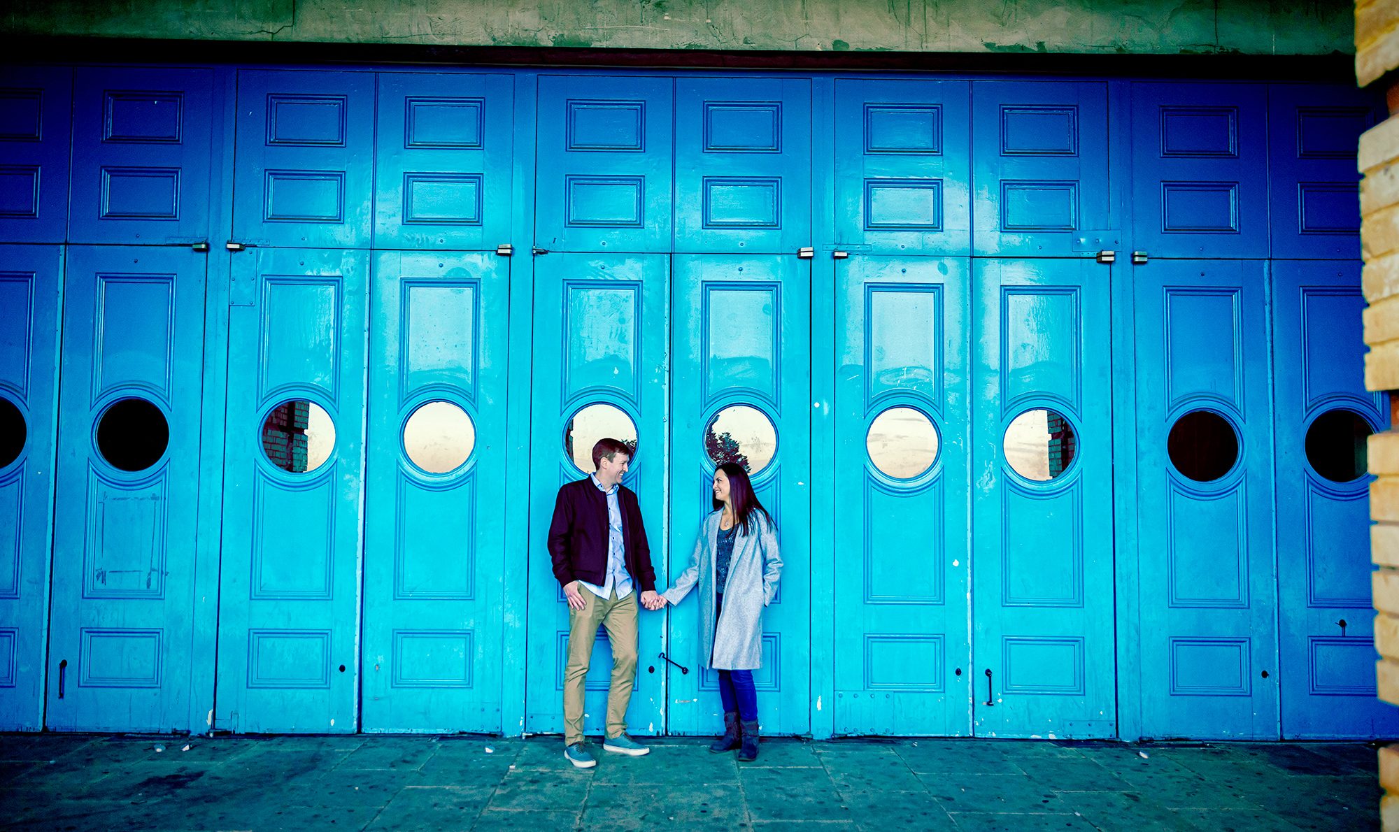 Engaged couple in front of blue doors Alexandra Palace wide shot